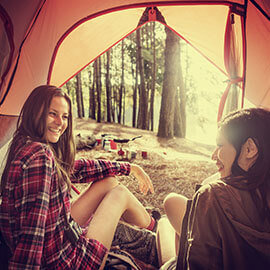 Two women in a tent looking out at their campsite