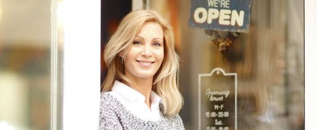 A business owner at the front door of her open establishment