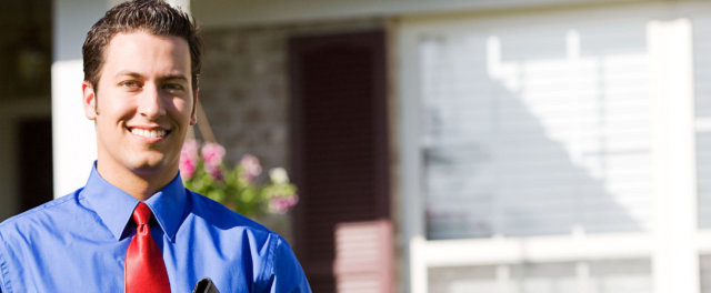 A man standing in front of a house wearing a blue dress shirt and a red tie