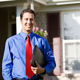 A man standing in front of a house wearing a blue dress shirt and a red tie