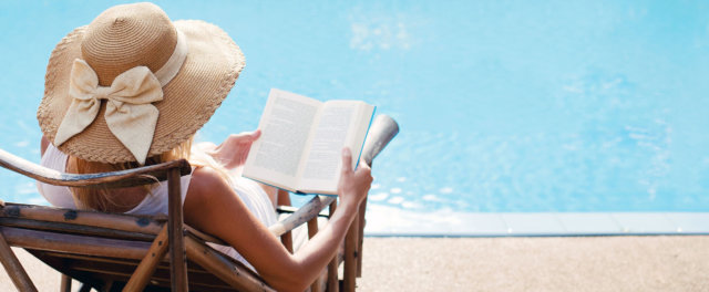 A woman in a hat reading a book poolside