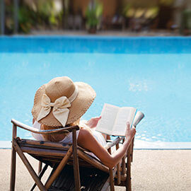 A woman in a hat reading a book poolside