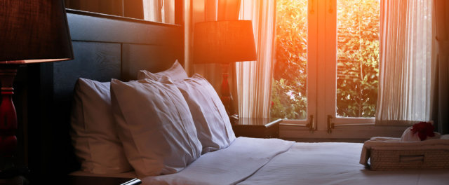 Sun shining in though a window on a made bed at a hotel