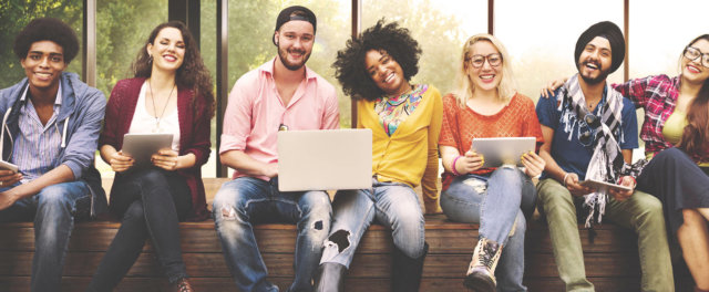 A diverse group of young people sitting on a bench with laptops and iPads