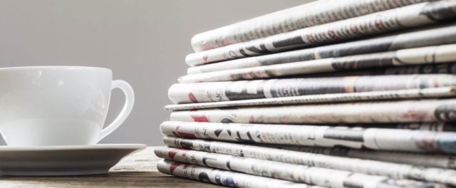 A stack of newspapers and a cup of coffee